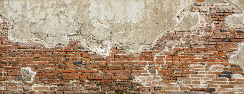 A weathered, old brick wall with patches of crumbling plaster and exposed red bricks, showing signs of age, decay, and erosion.