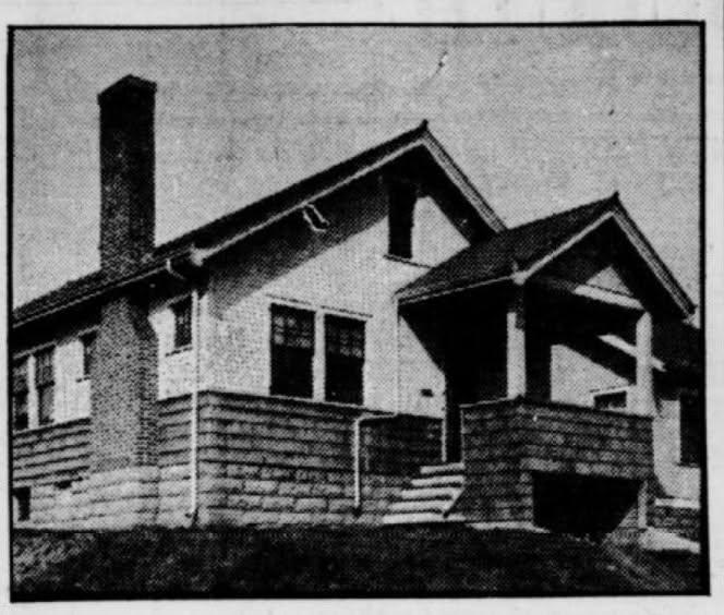 Black and white photo of a small house with a chimney, covered porch, sloped roof, and steps leading to the front door. The house sits on a raised foundation with siding and several windows visible.